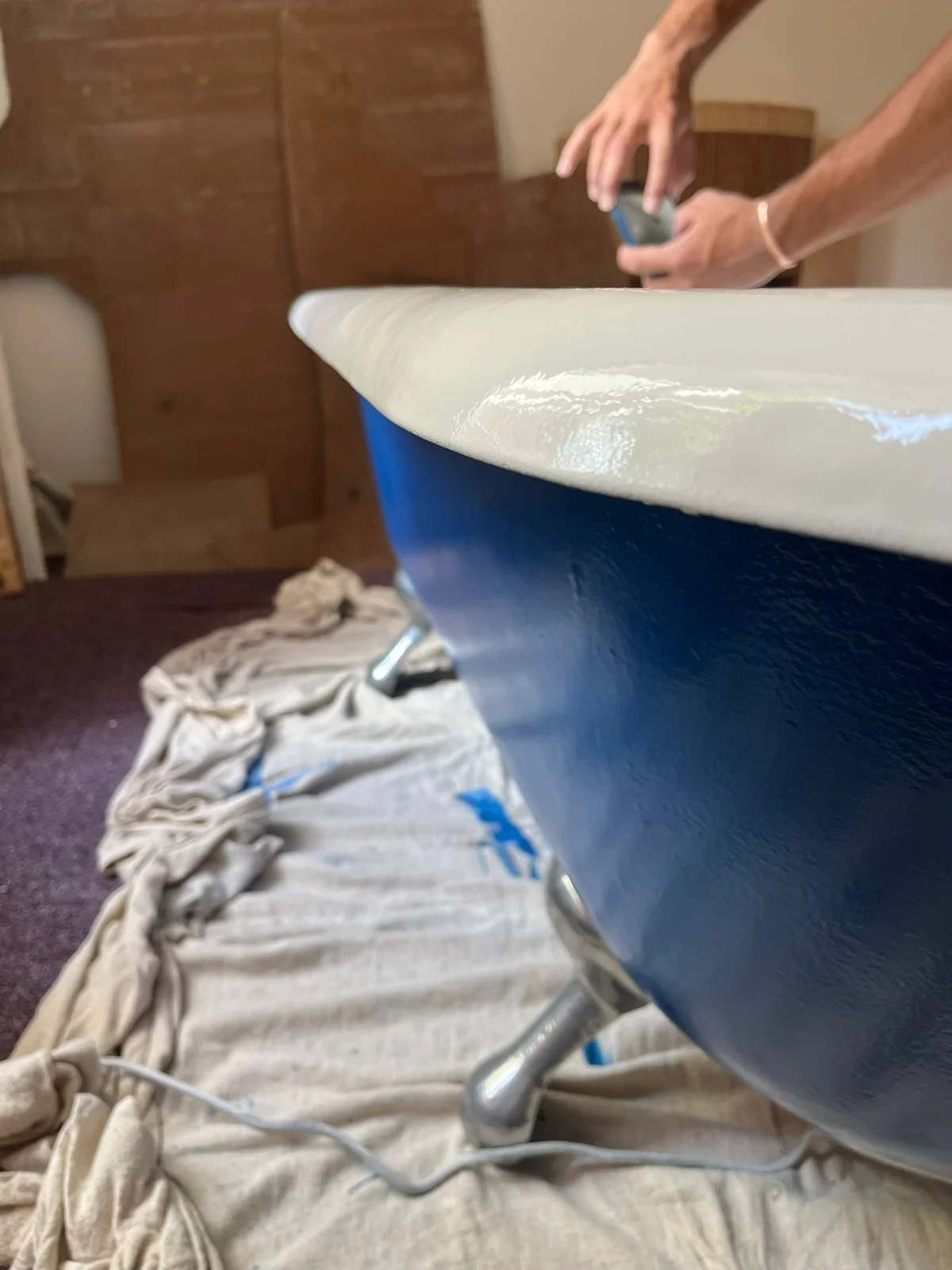 Hands working along the rim of a blue freestanding bath